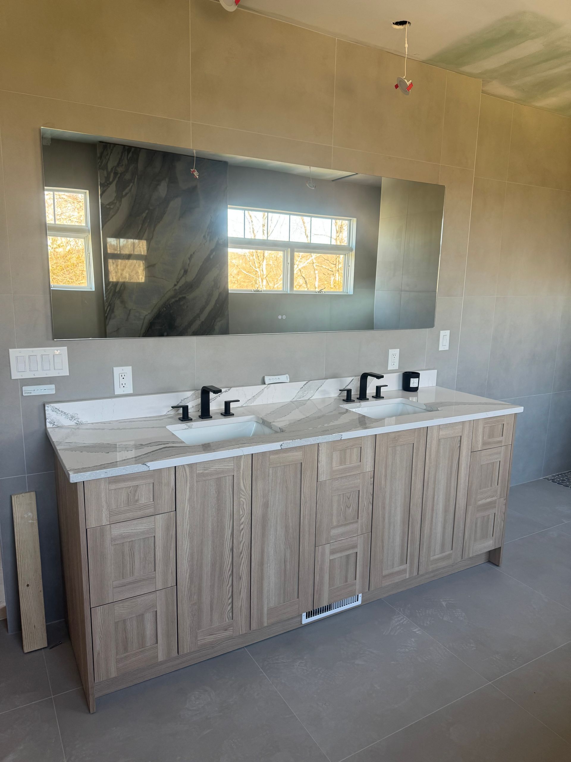Bathroom with double vanity, large mirror, and black faucets. Construction in progress.