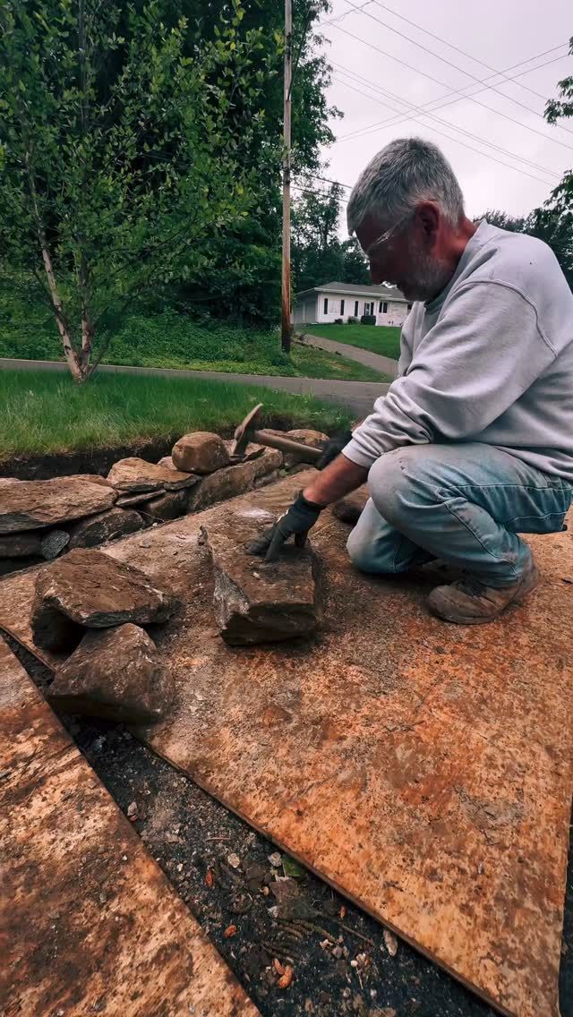 Man placing rocks, working on a stone wall. Outdoors, sunny day.