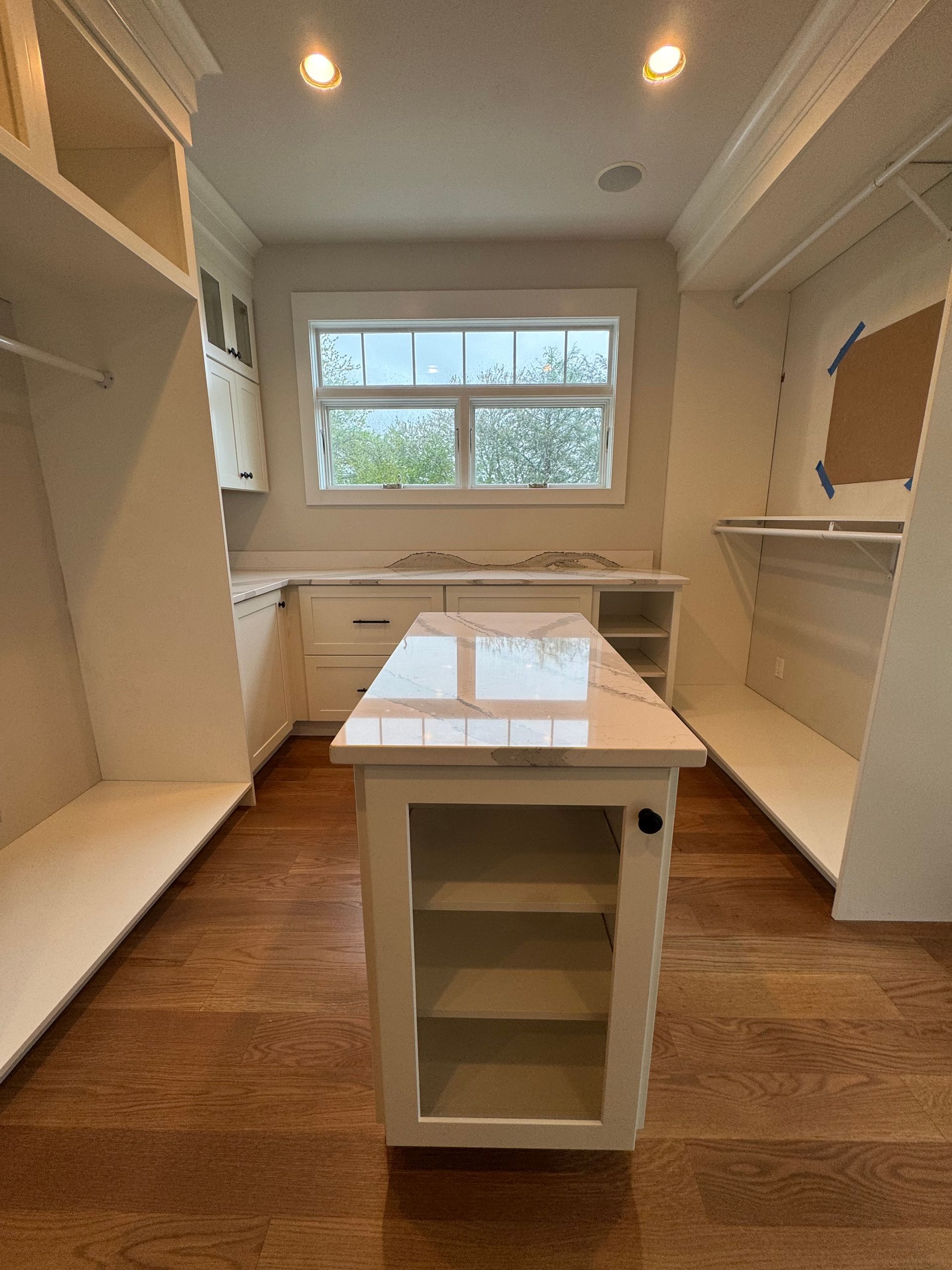 Walk-in closet with white cabinetry, wood flooring, and an island. The window provides natural light.