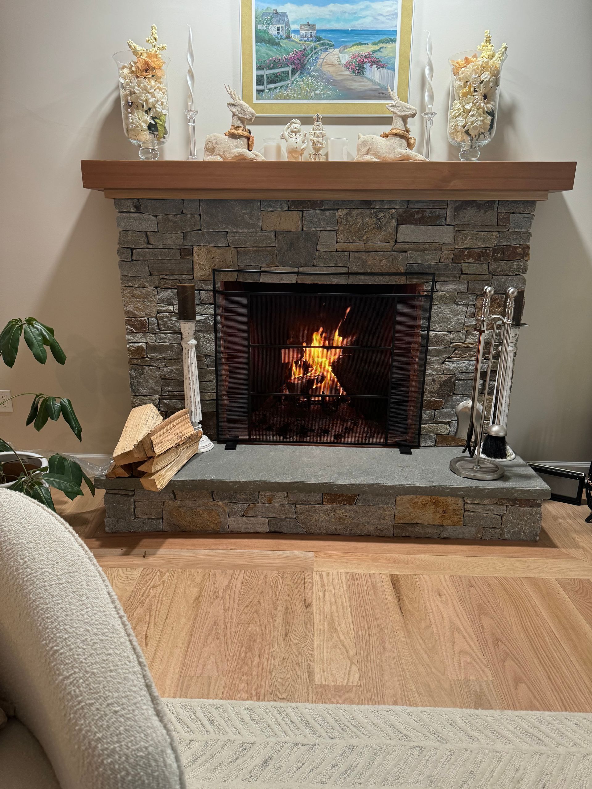 Fireplace with burning fire, stone surround, wood mantel, and wooden floor.