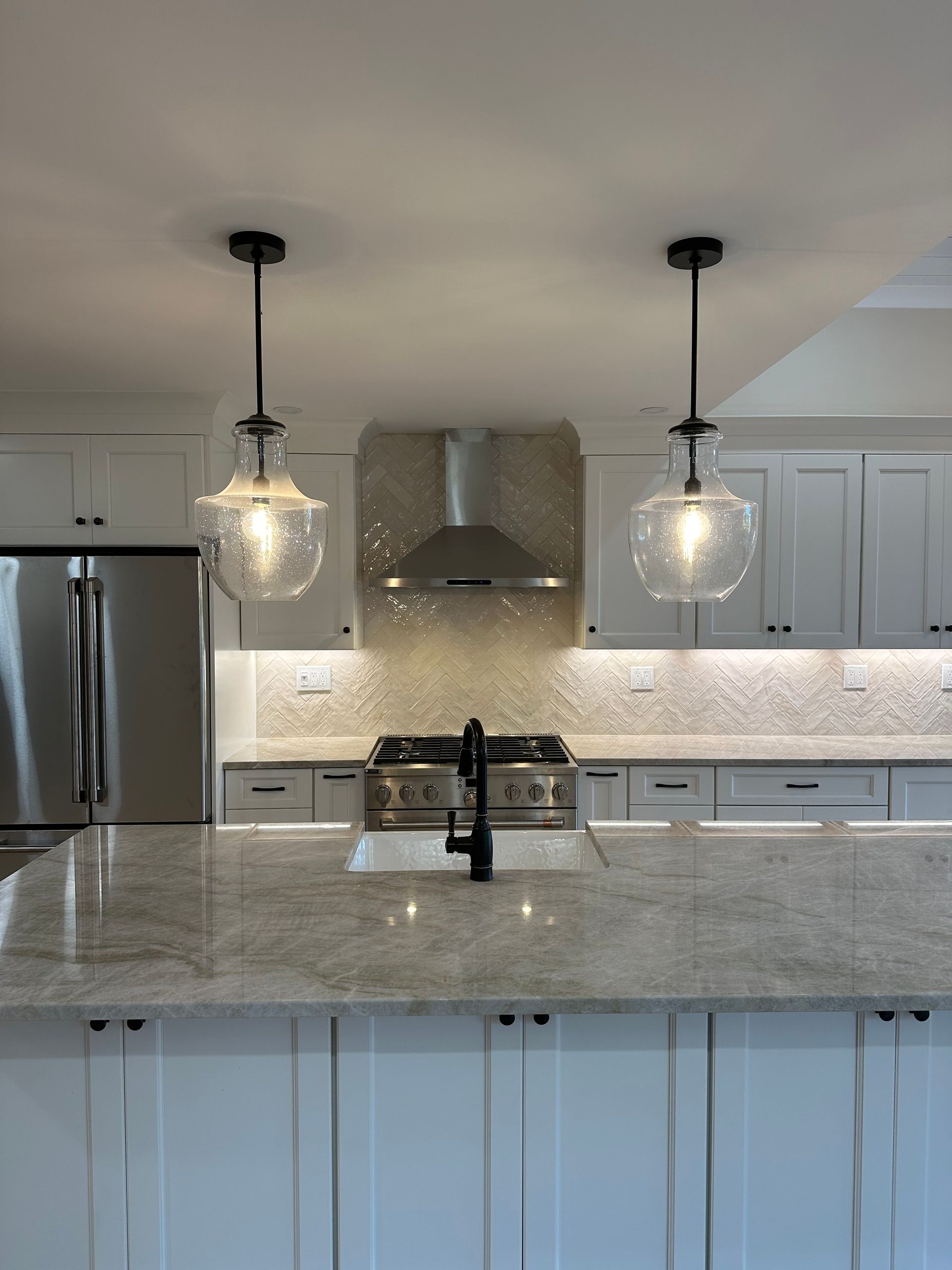 Kitchen with white cabinets, granite countertop, two pendant lights, and stainless steel appliances.