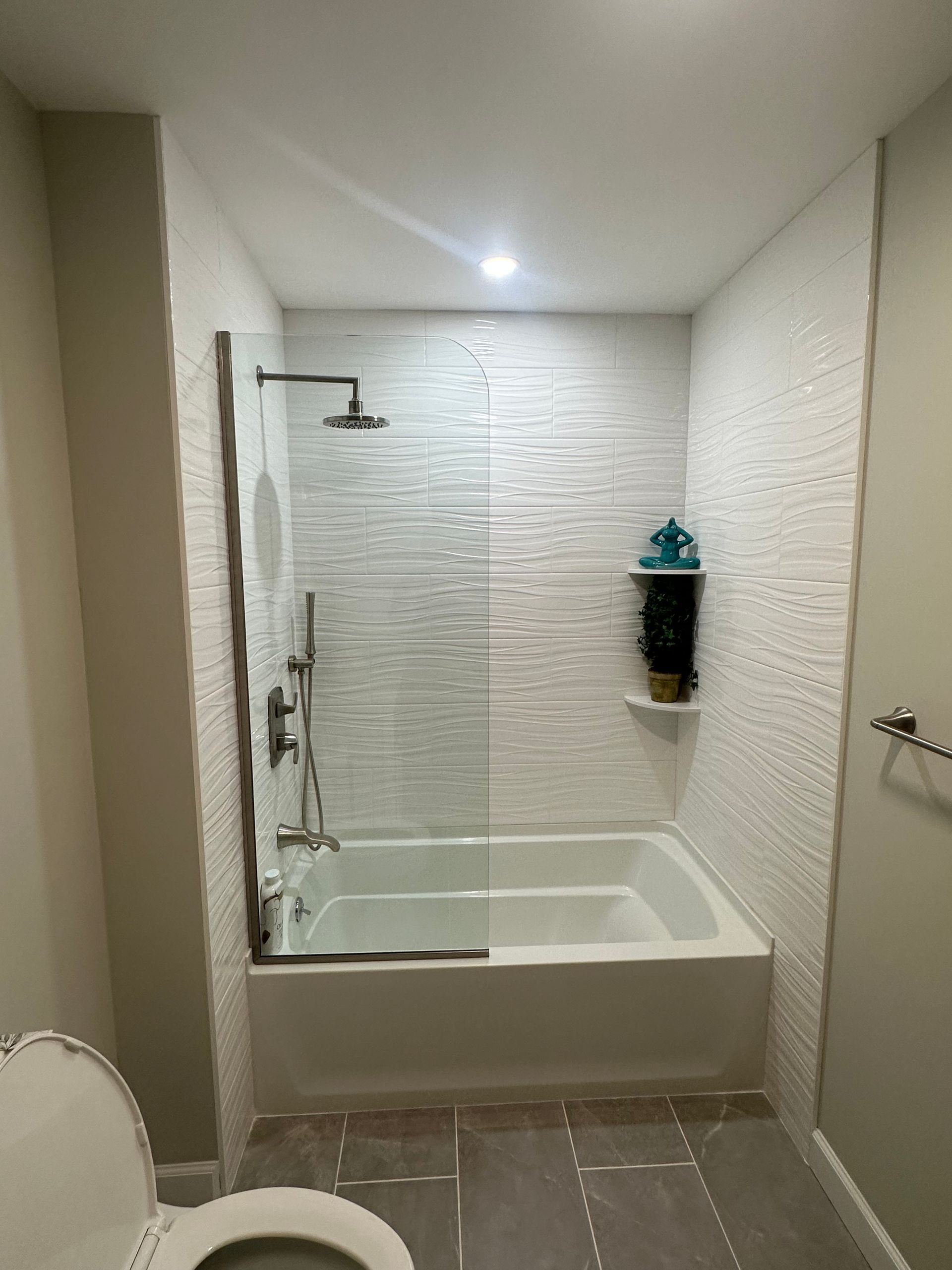 Modern bathroom with a white bathtub and textured white tile walls, a glass shower door.
