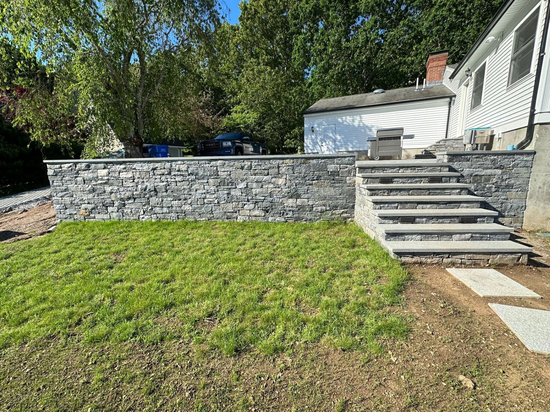 Stone retaining wall with steps, freshly laid grass, and a white house in the background.