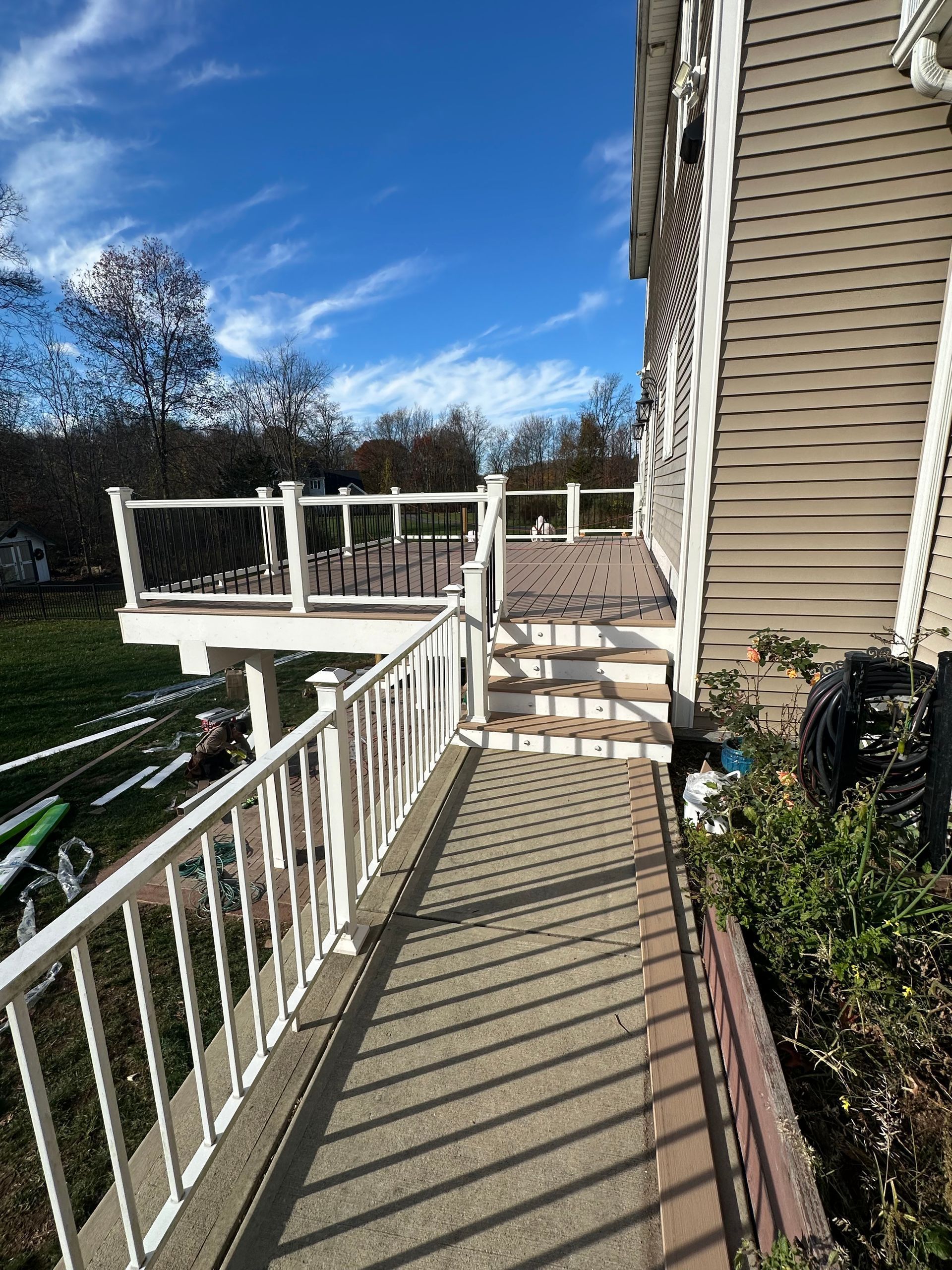 White-railed ramp leads to a multi-level deck, with stairs to upper levels, next to a beige house, under a blue sky.