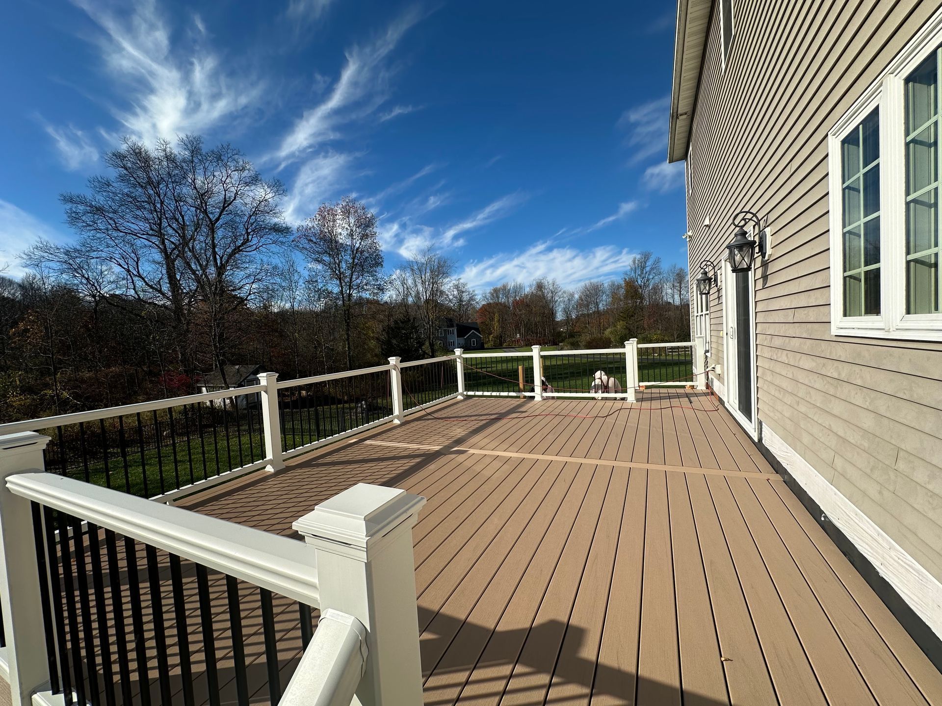 Wooden deck attached to a house with white railing. Clear, blue sky with wispy clouds.