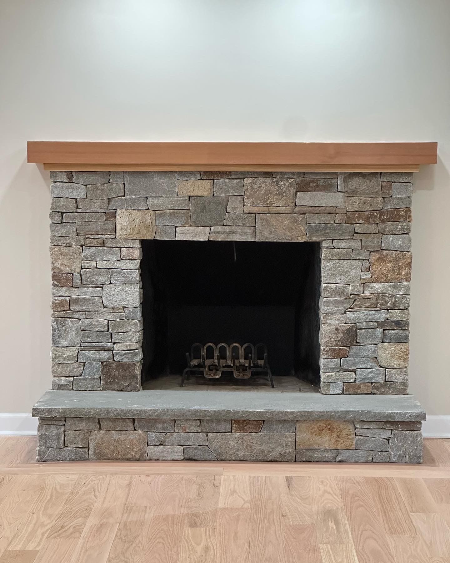 Stone fireplace with wooden mantel, set against a white wall. Light wood flooring visible.
