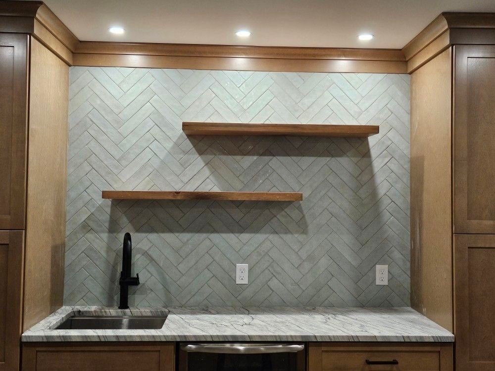 Bar area with light blue herringbone tile backsplash, wooden shelves, and granite countertop.