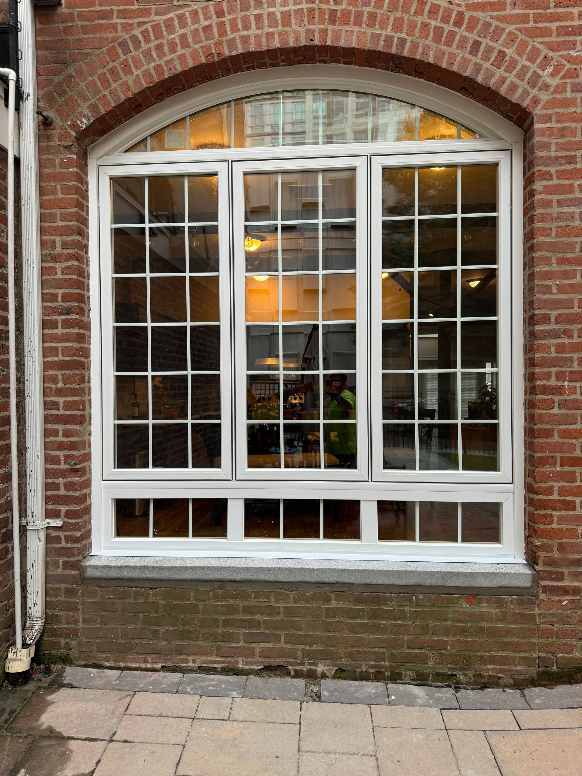White framed window with many panes, set in a brick building.