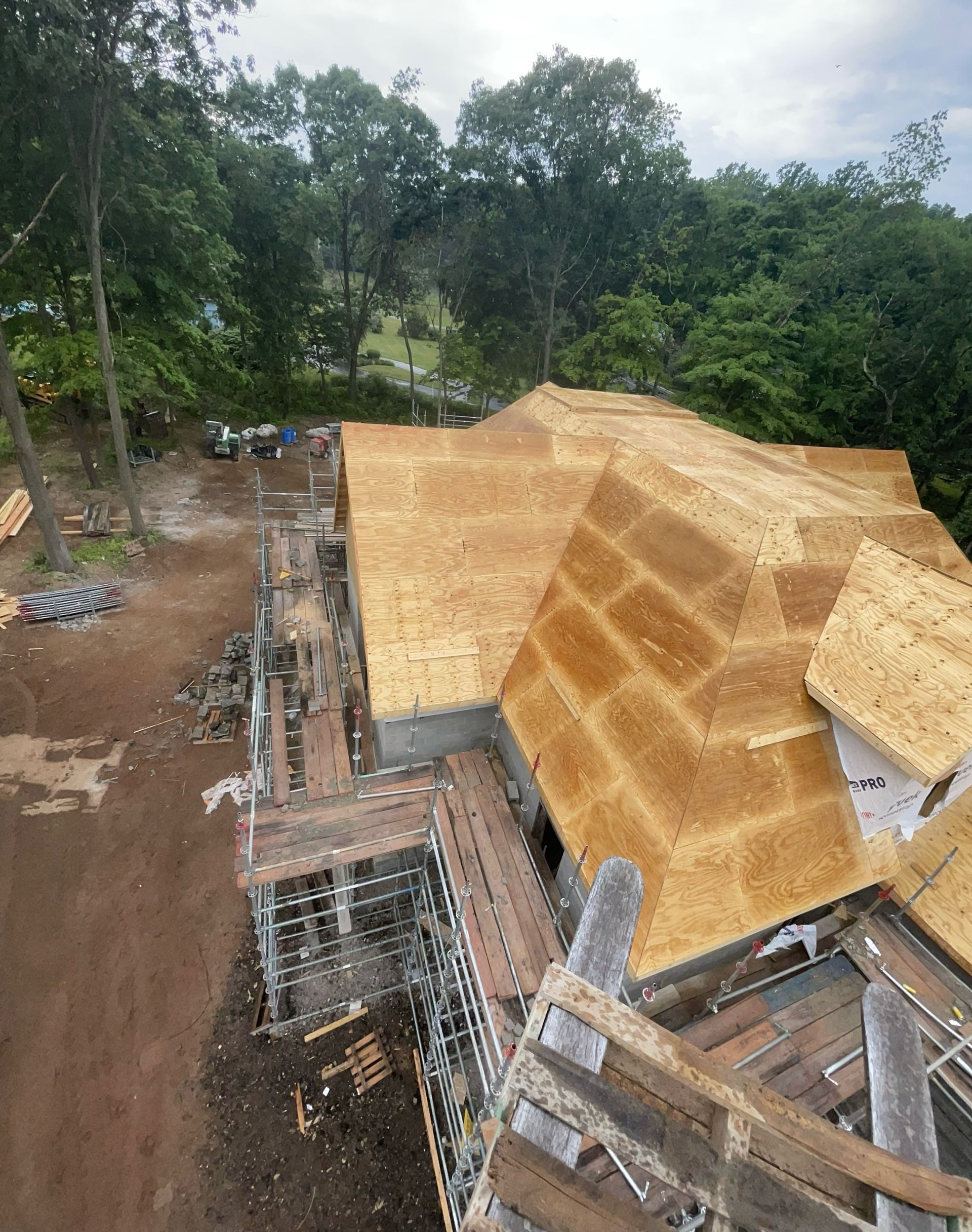 Construction site, partially roofed house with scaffolding. Trees in background, overcast day.