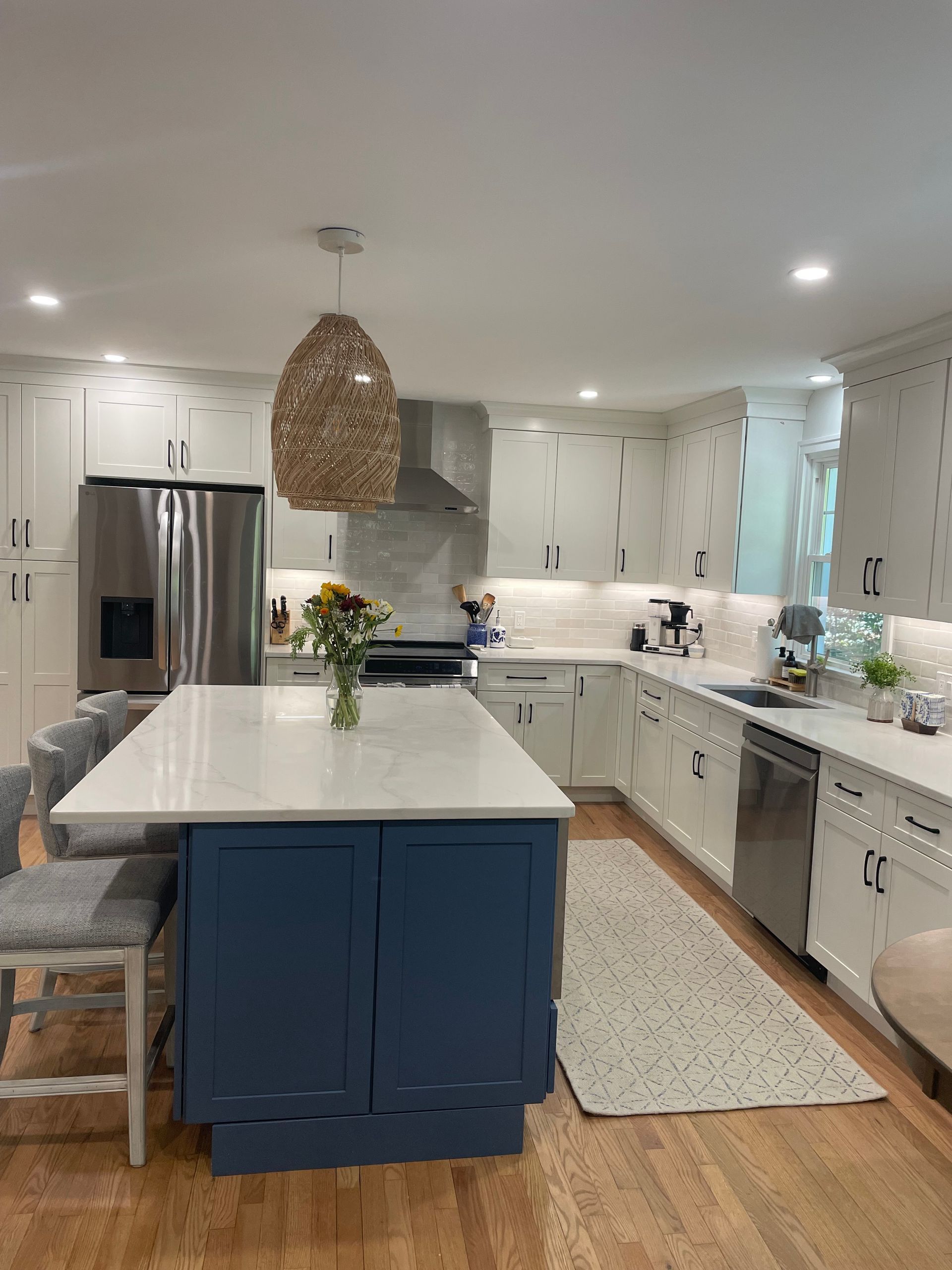 White kitchen with blue island, pendant light, stainless steel appliances, and hardwood floors.