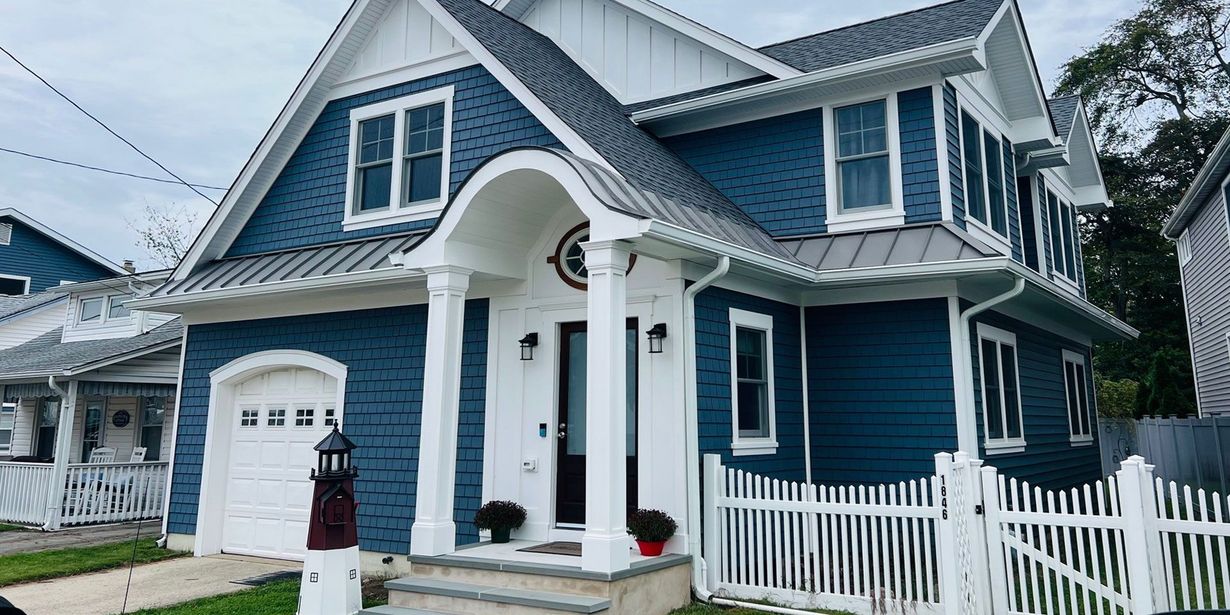 Blue two-story house with white trim, arched porch, and white picket fence