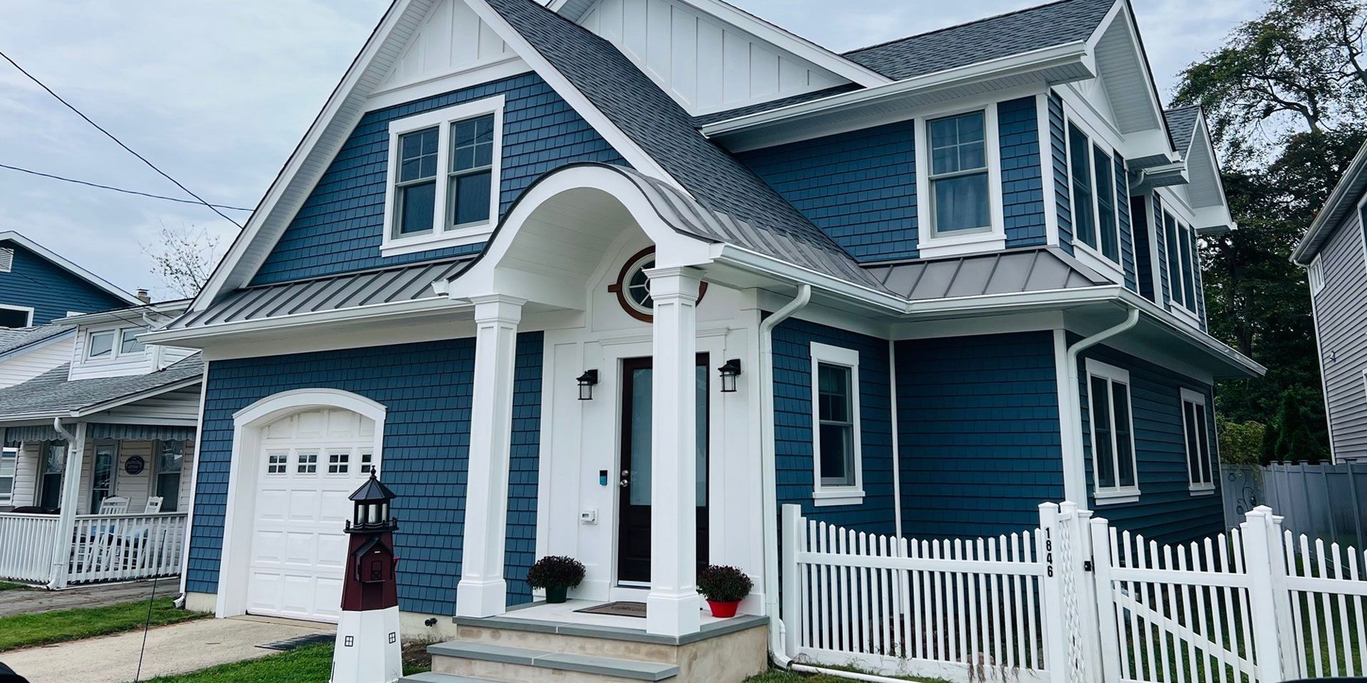 Blue two-story house with white trim, arched porch, and white picket fence