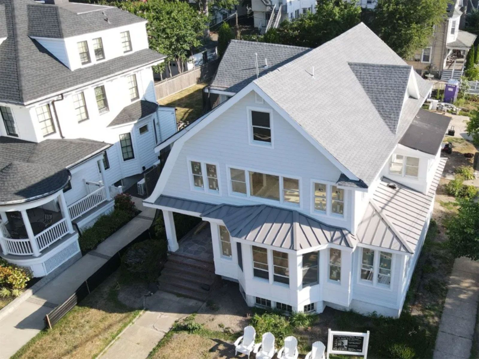 Aerial view of a white house with a gray roof, porch, and backyard patio chairs