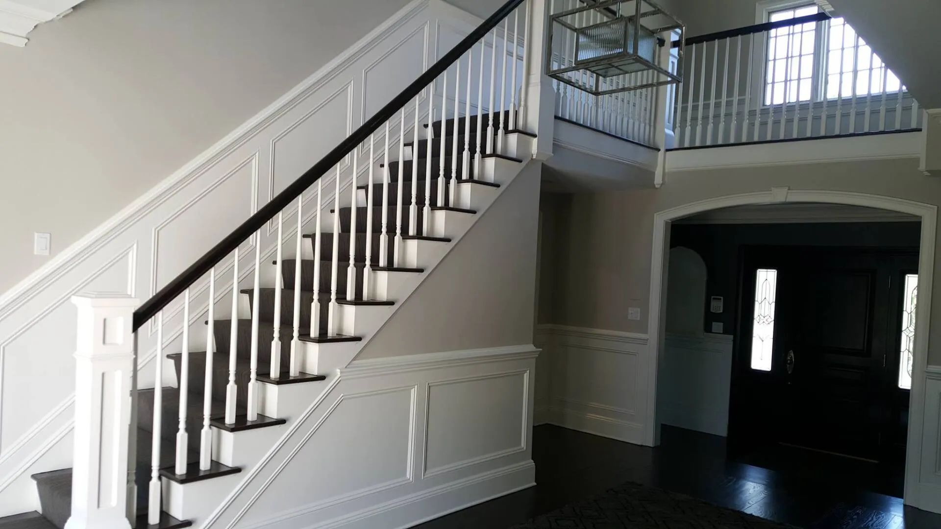 Interior staircase with white balusters and dark handrail, beside a dark entryway and windowed landing