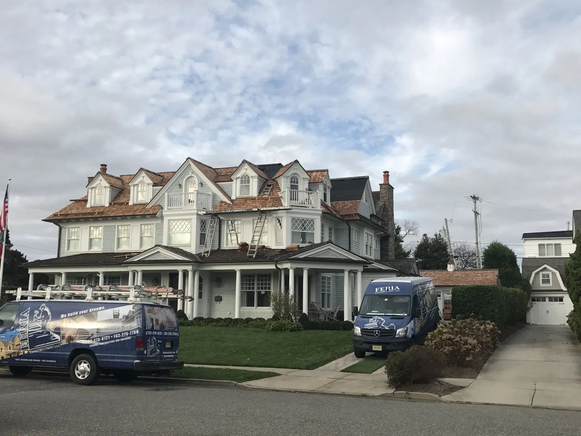 Large white Victorian house with wraparound porch, parked vans, and cloudy sky.