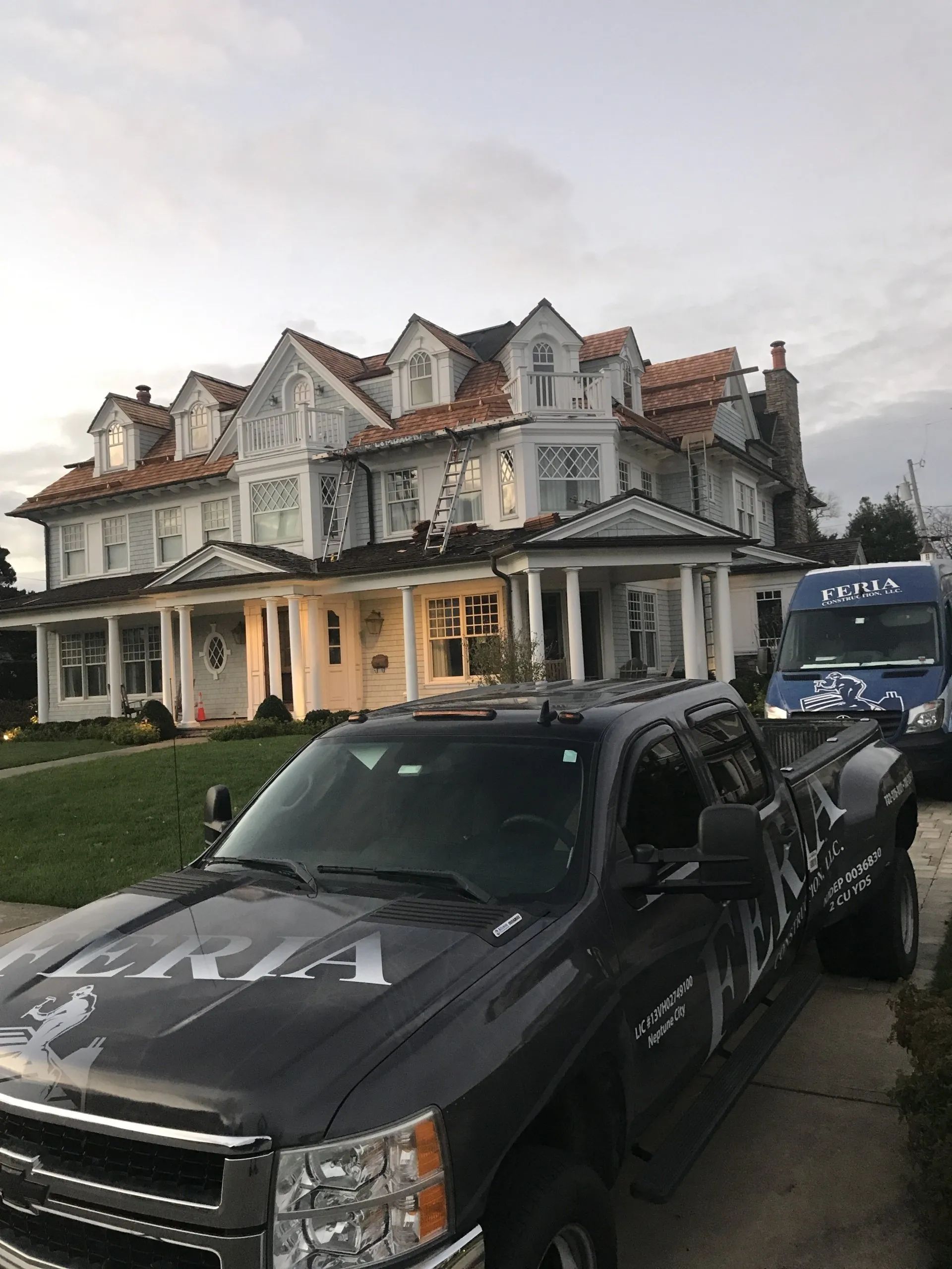 Black pickup truck parked on a street in front of a large old house with a blue van behind it.