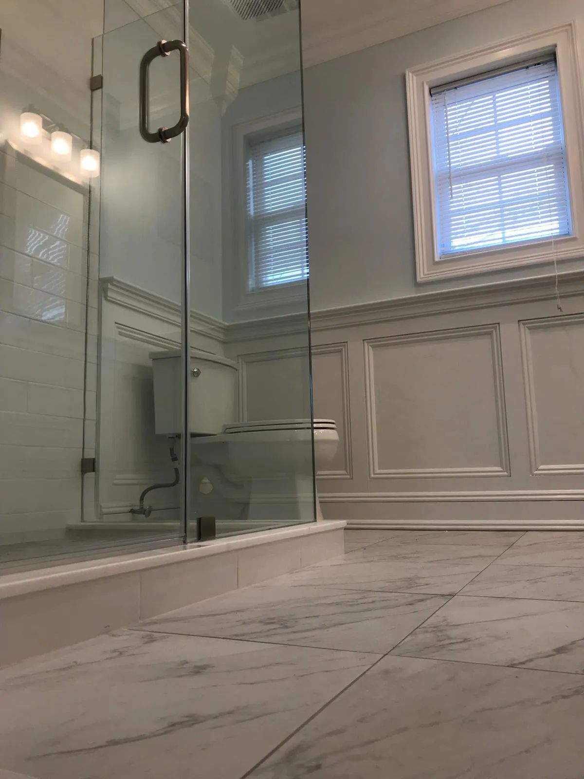Modern bathroom with a glass shower, marble tile, and frosted windows.