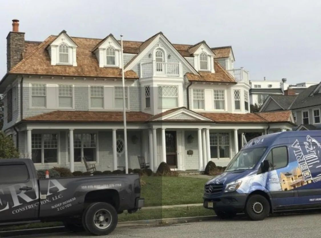 Large white Victorian house with porches, viewed from the street with parked vans in front.
