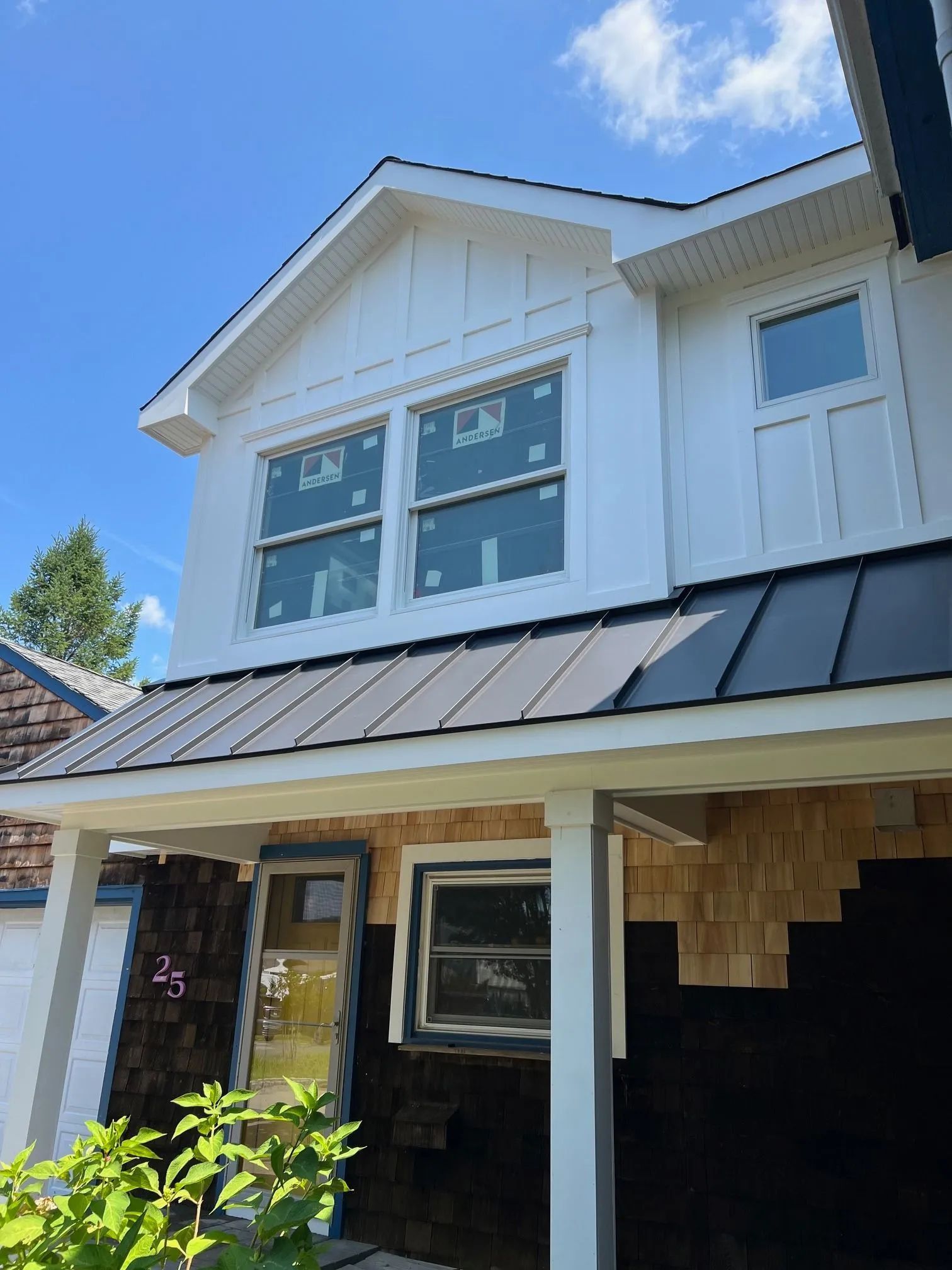 White two-story house exterior with black metal roof and front porch under a blue sky