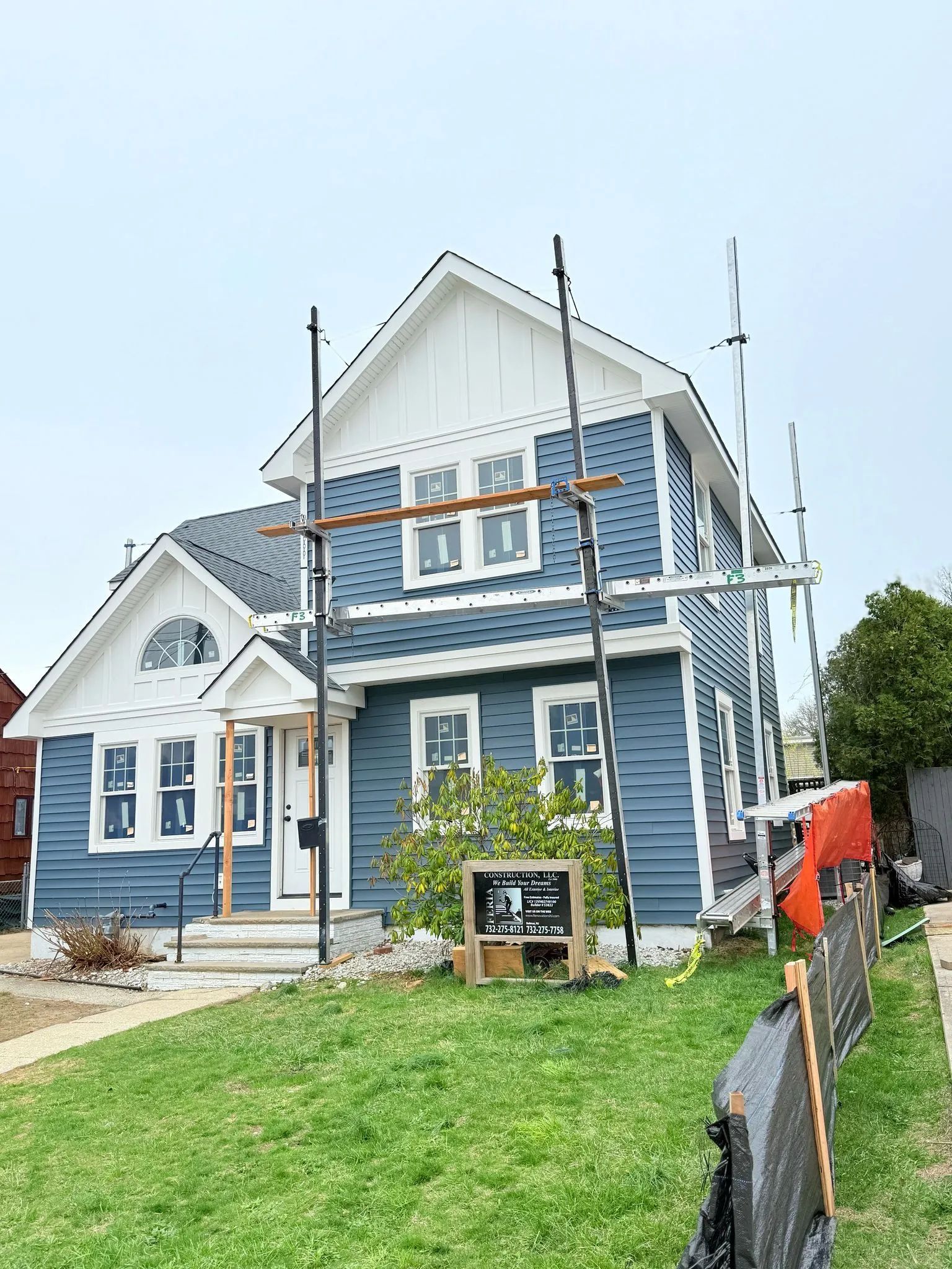 Blue house with white trim under renovation, with scaffolding and a small front yard.