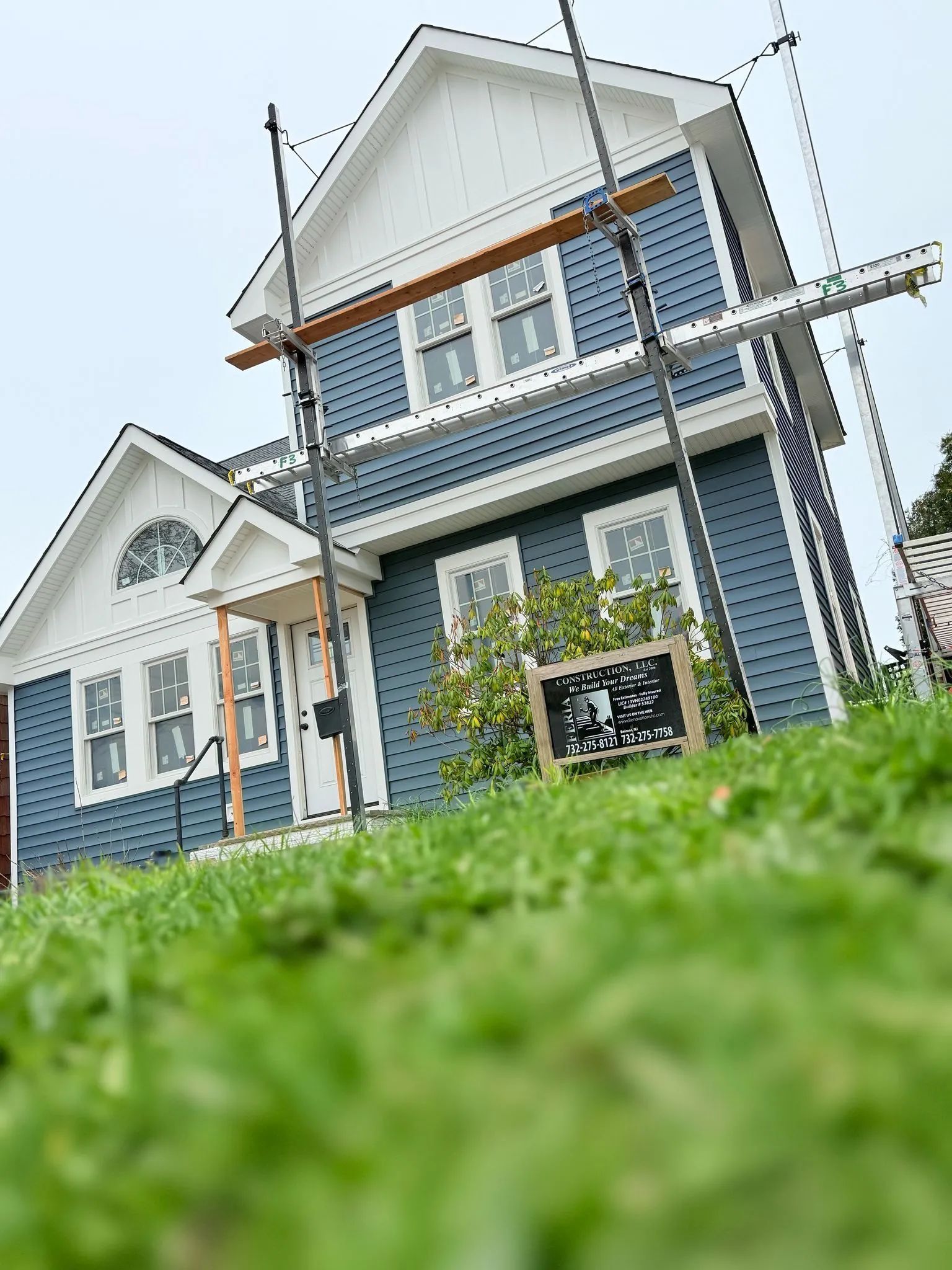 Blue-and-white two-story house with porch, viewed from low angle through green grass