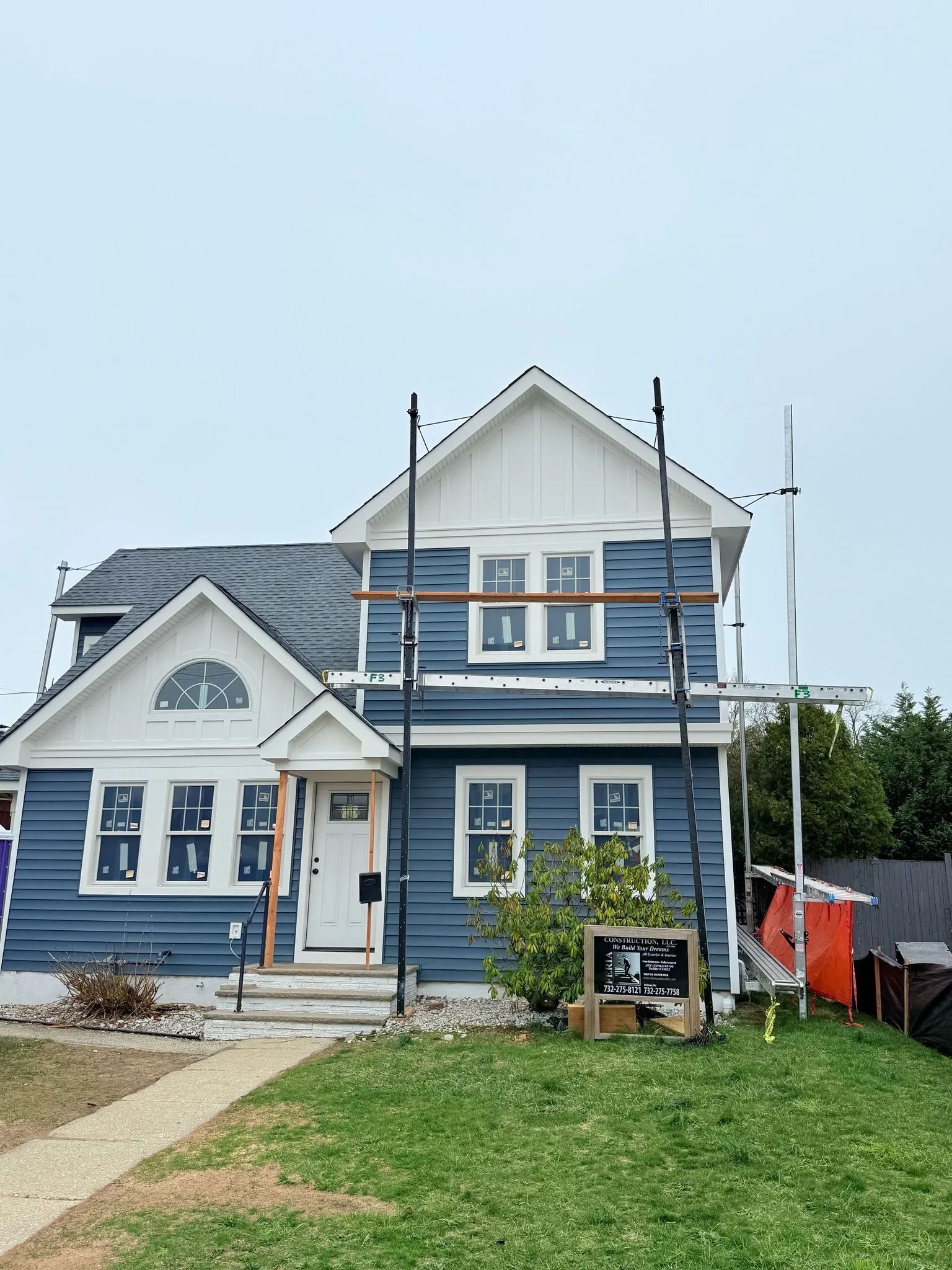 Blue house with white trim under construction, with scaffolding and a small front lawn.