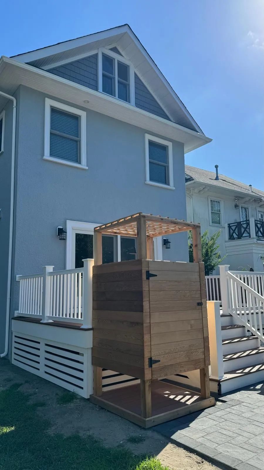 Backyard deck with a wooden compost bin beside a light gray house and white fence