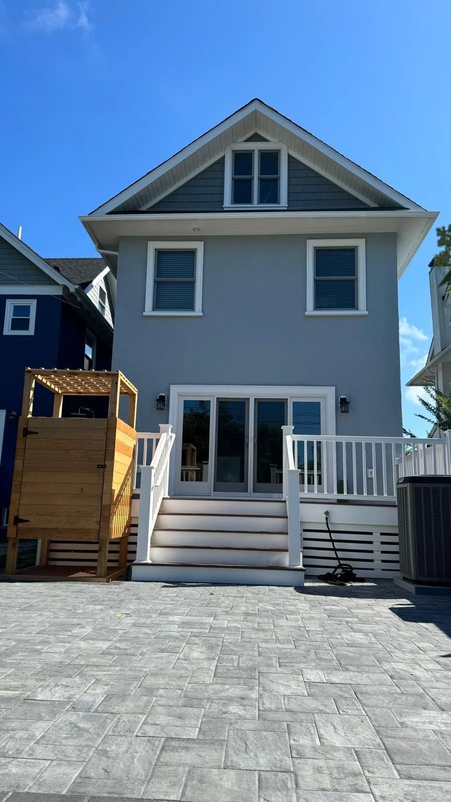Gray two-story house with white trim, front steps, and a small wooden deck beside a paved driveway.