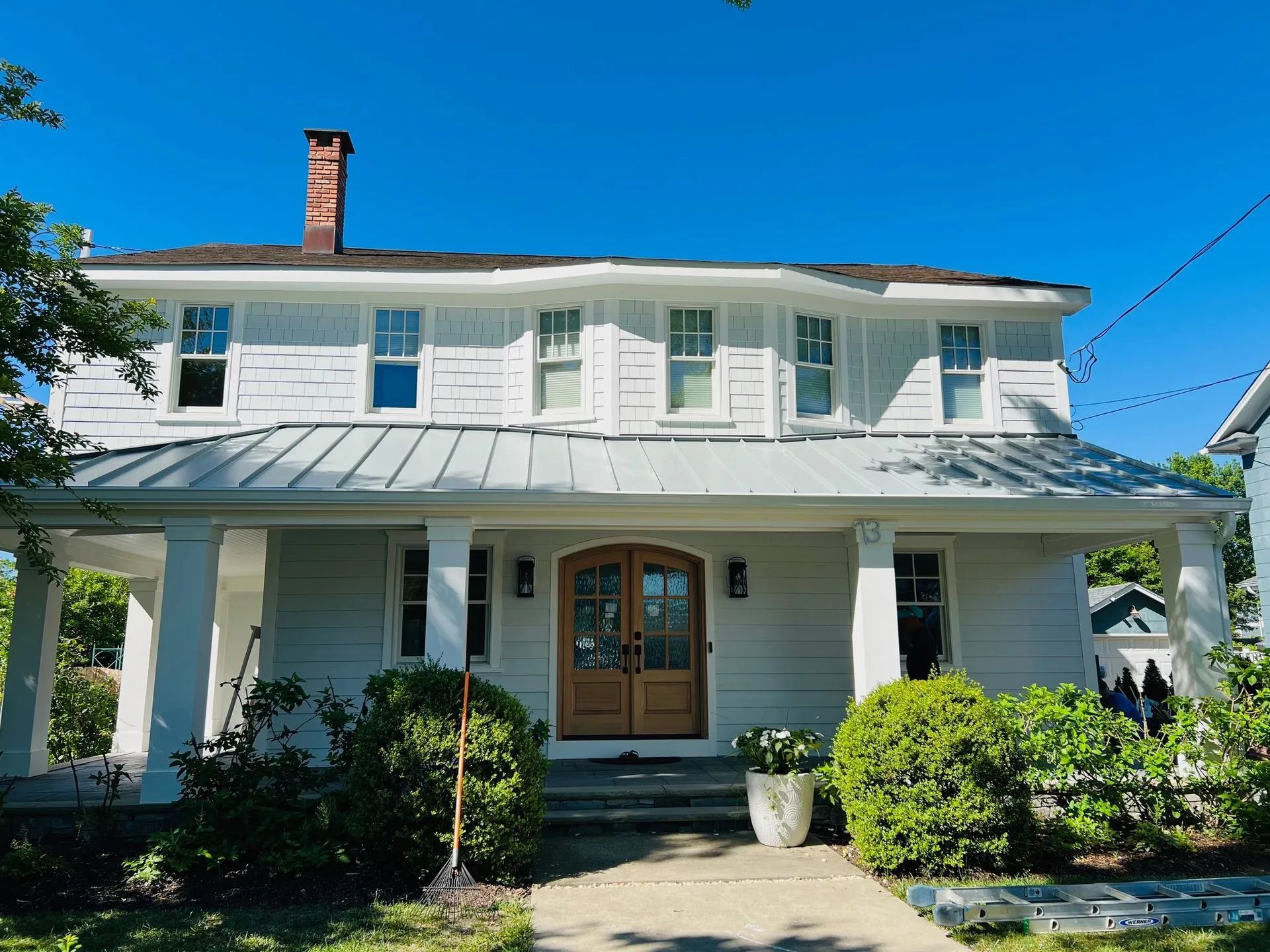 White two-story house with a porch, teal shutters, and a brick chimney under a blue sky