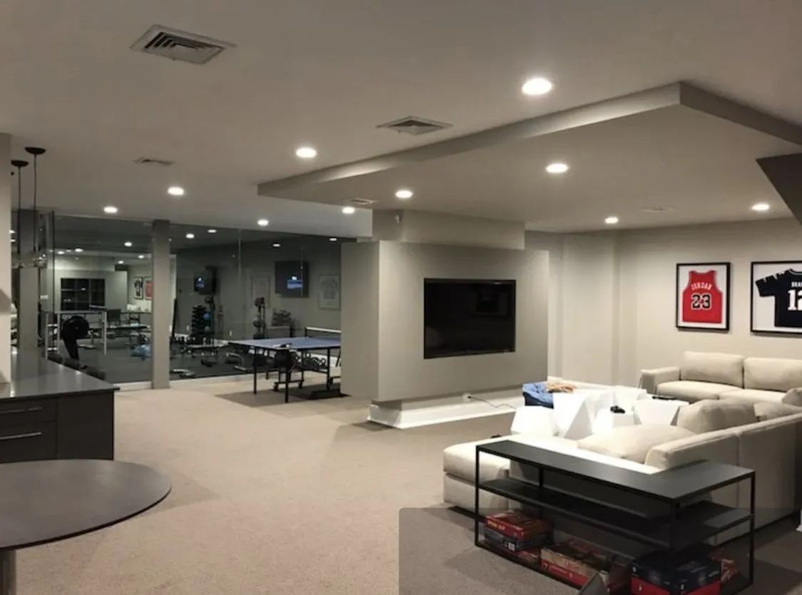 Modern office lounge with a TV, sofa, coffee table, and glass-walled meeting room.