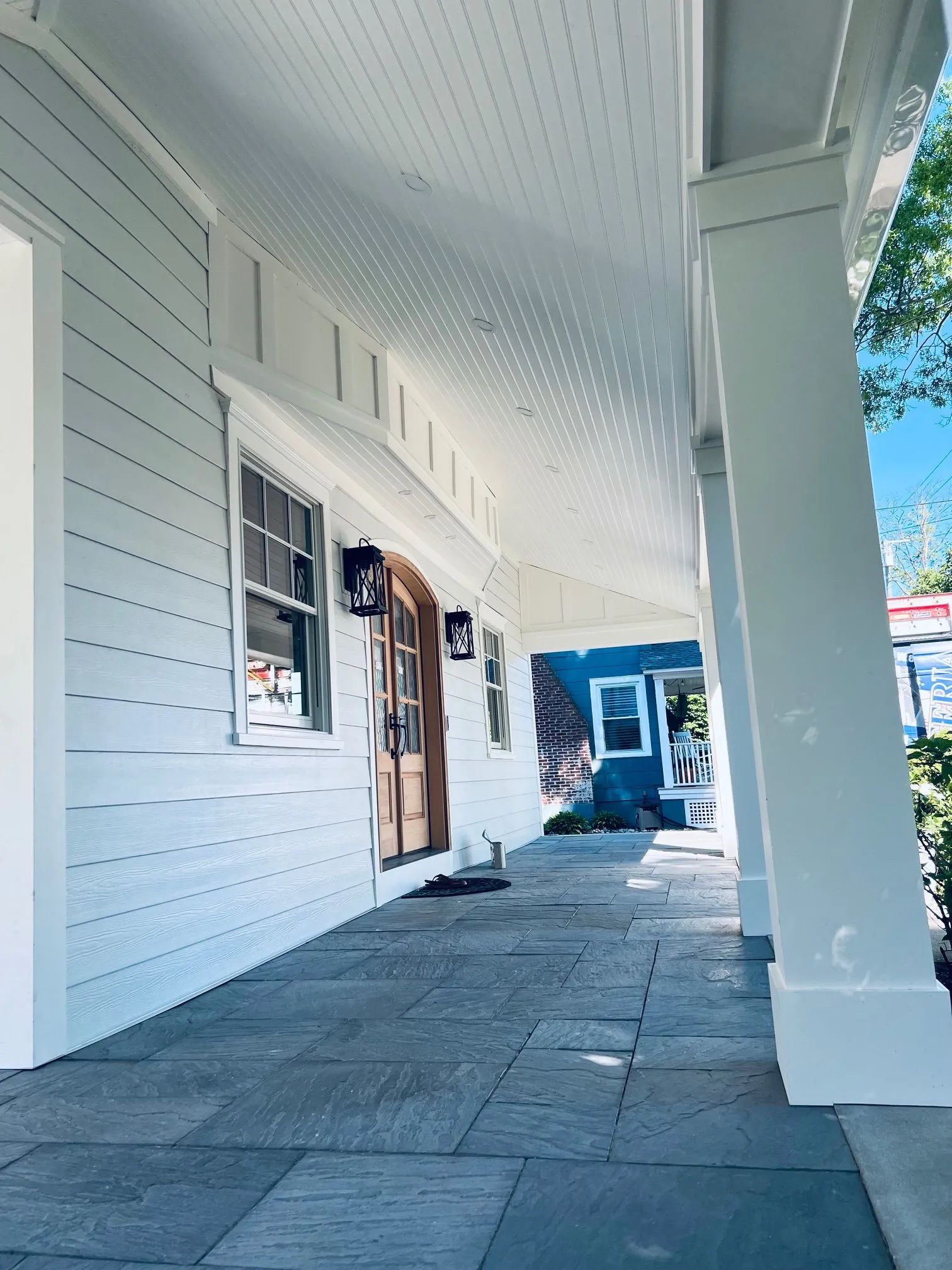 Covered white porch with stone floor, columns, and storefront windows in bright daylight.