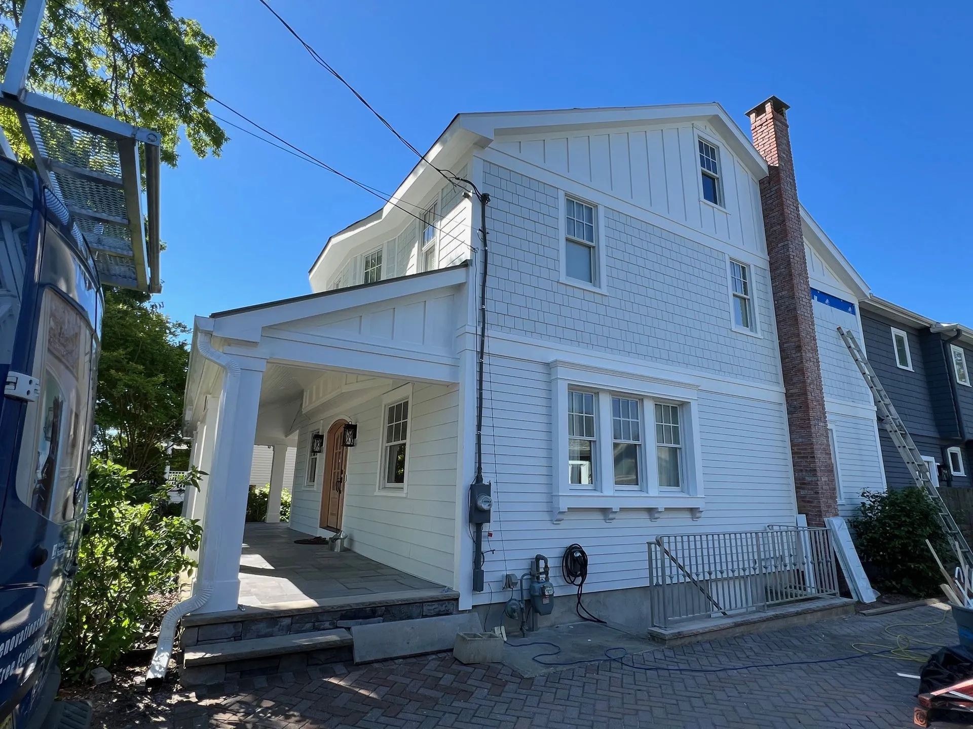 White two-story house with a covered porch and a bicycle leaning against the side on a sunny street.