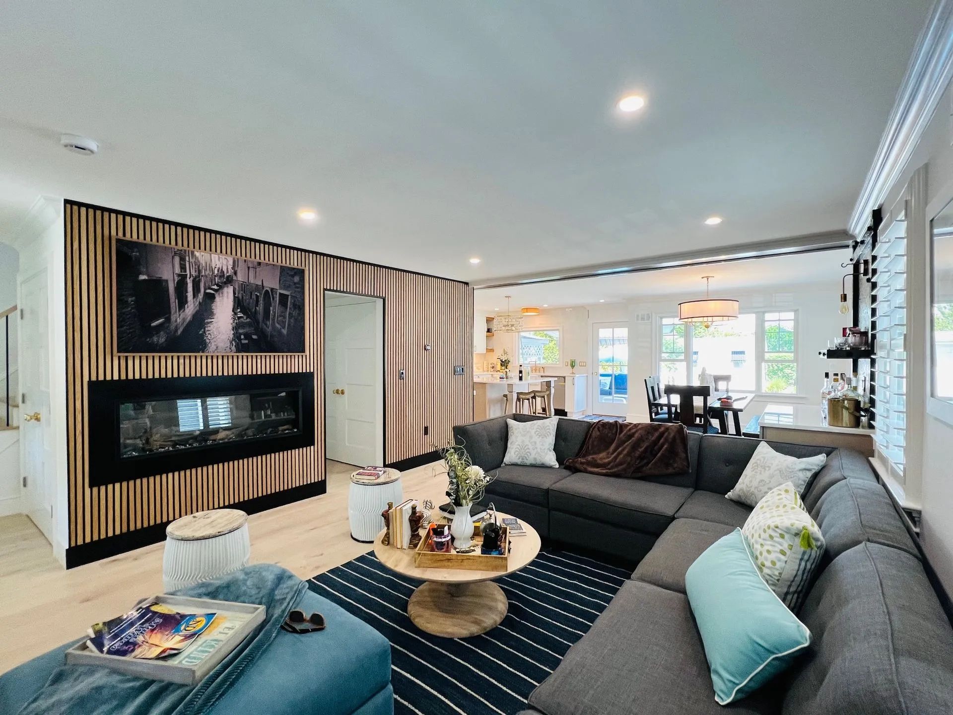 Bright living room with sectional sofa, fireplace, striped accent wall, and dining area in the background