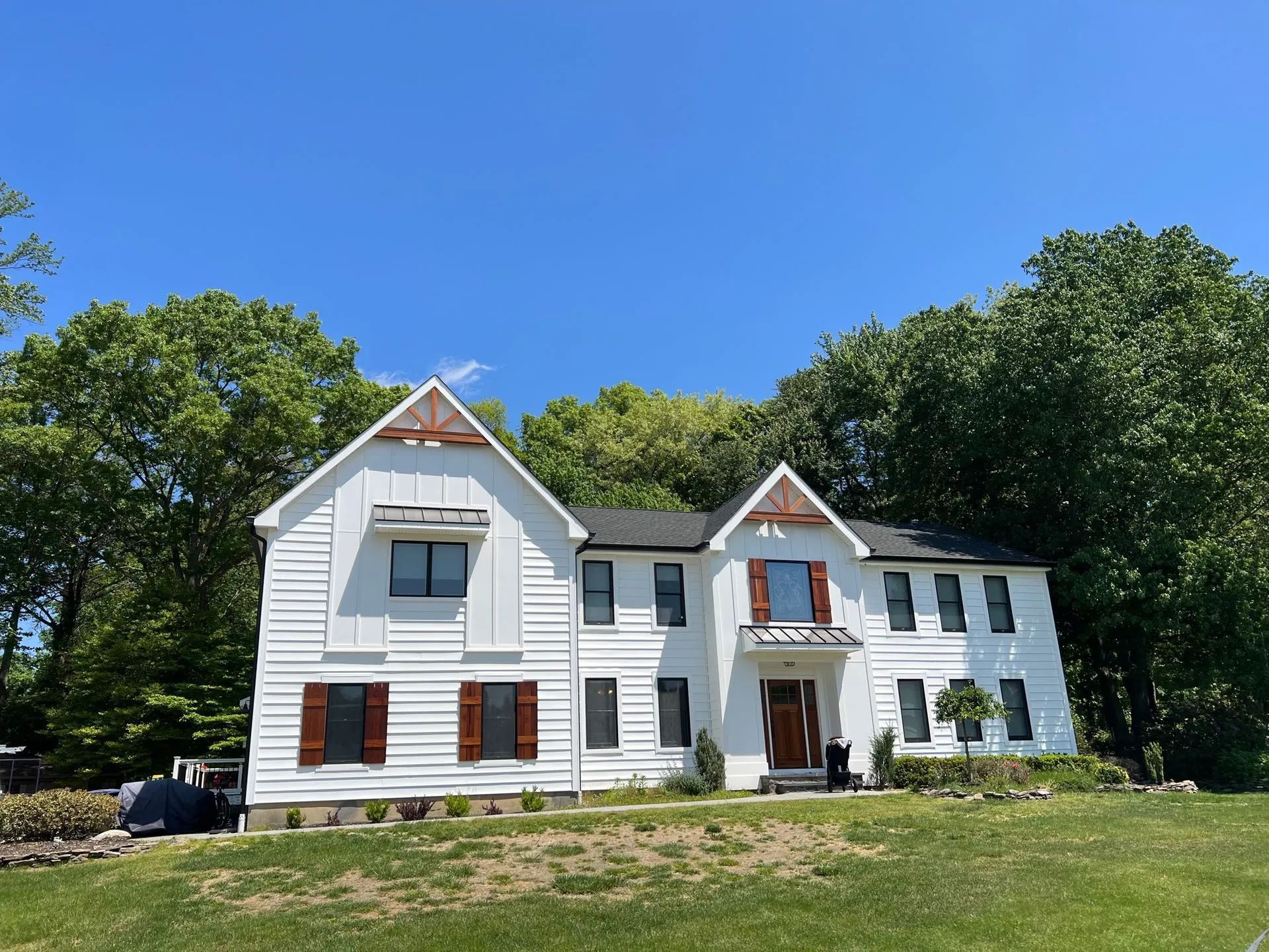 White two-story house with red shutters and gables, set on a grassy lawn under a blue sky