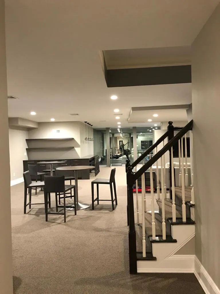 Basement living area with carpet, bar stools, kitchen counter, and staircase railing.