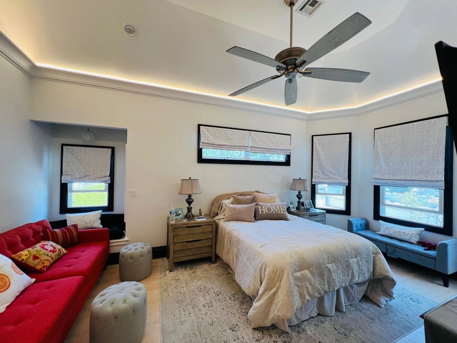 Bright bedroom with a bed, red sofa, windows, ceiling fan, and light decor