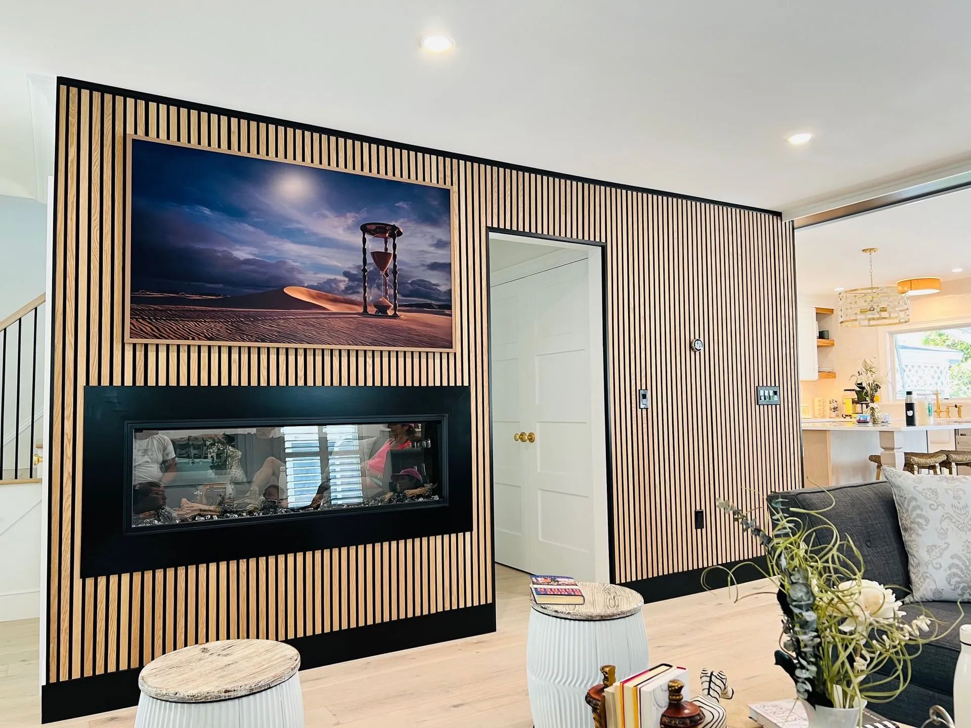 Modern living room with striped wood accent wall, framed fireplace, and sunset wall art