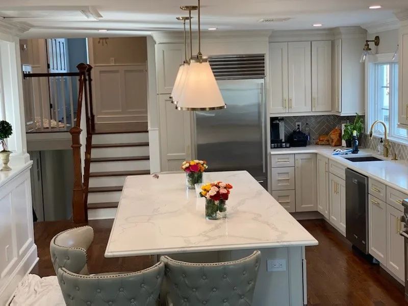 Bright white kitchen with island, hanging pendant light, stainless fridge, and flowers on the counter
