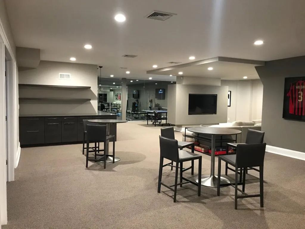 Empty modern lounge with chairs, tables, black cabinets, and wall art under recessed lighting