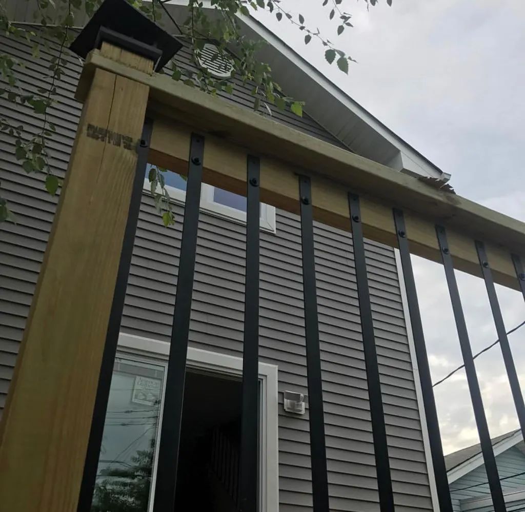 Modern house exterior with wooden posts, black railings, and an open doorway under a cloudy sky