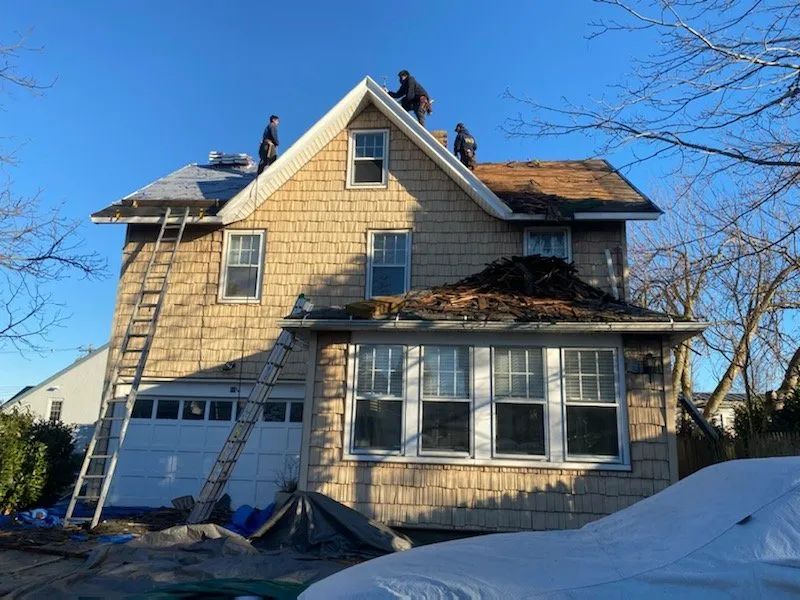 Damaged house with missing roof sections and a ladder leaning against the front in winter snow