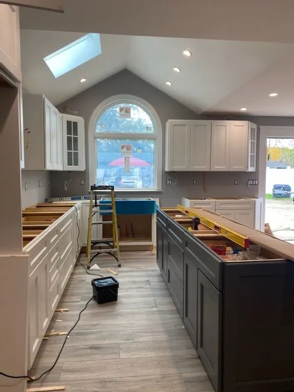 Kitchen renovation in progress with cabinets, tools, and a ladder under a vaulted ceiling and arched window