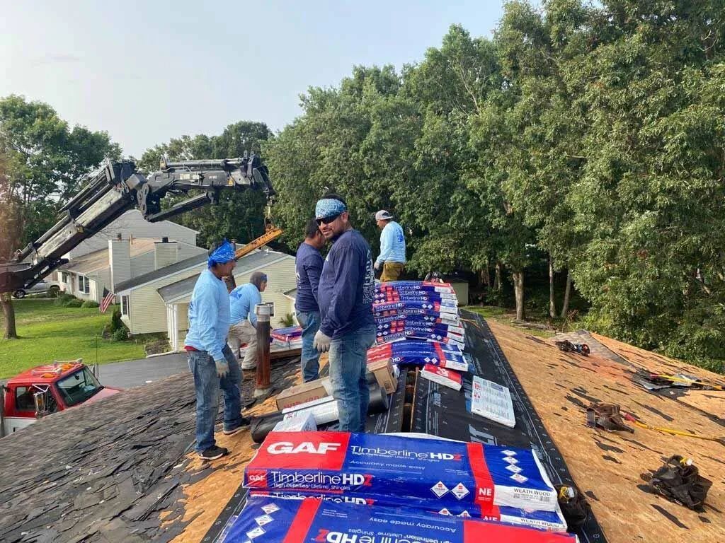 Workers loading red and blue supply boxes onto a truck beside an orchard and crane truck