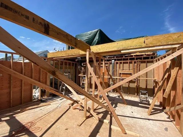 Framed house under construction with exposed wood beams and roof trusses under a blue sky