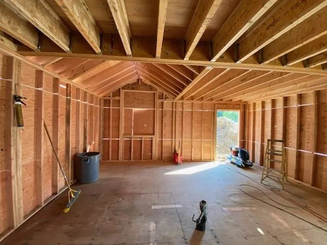 Unfinished wooden room under construction with exposed beams, plywood walls, and tools on the floor.