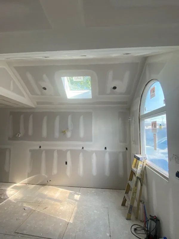 Drywalled room under construction with skylight, arched window, and a ladder against the wall.