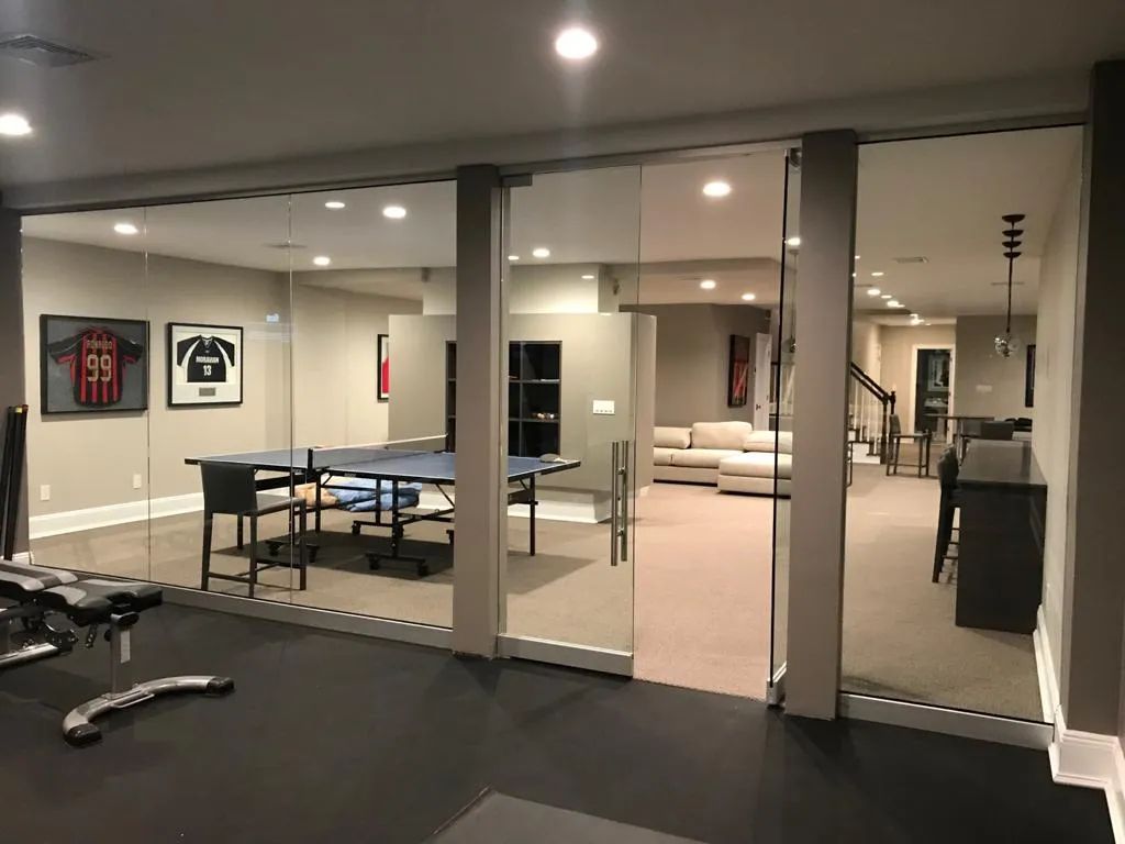 Modern basement recreation room with ping-pong table, glass wall, and home gym equipment