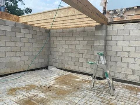 Partially built cinder block room with exposed roof beams and a ladder on the floor