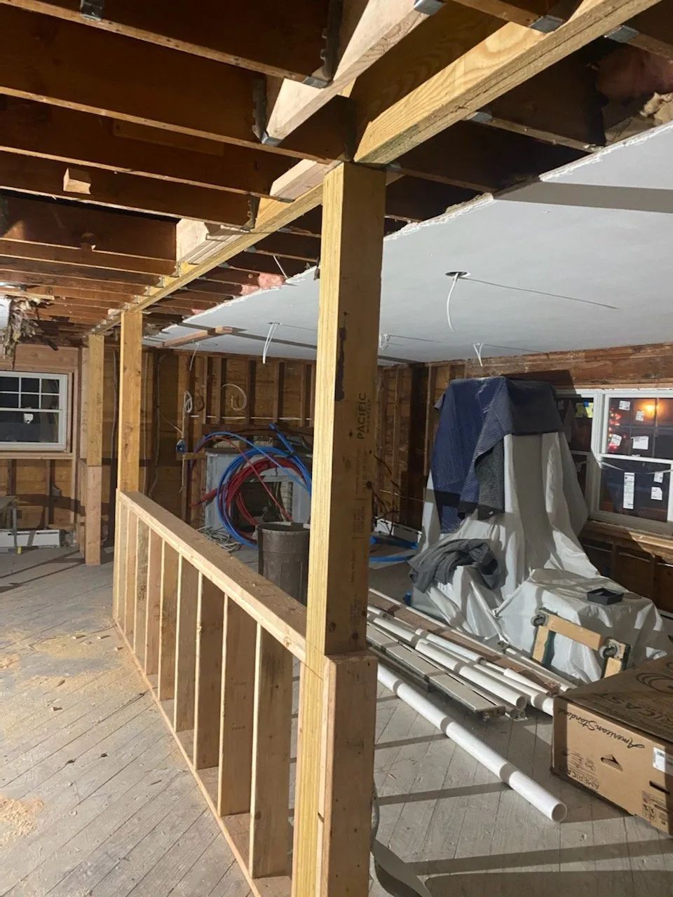 Basement under renovation with exposed beams, wooden railing, tools, ladders, and stored materials.