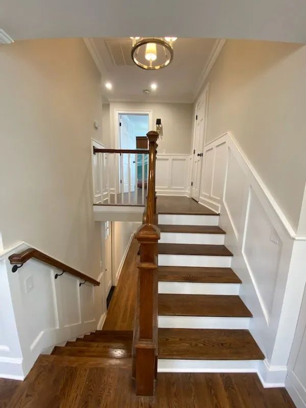 Staircase landing with white walls, dark wood railings, and a ceiling light in a narrow hallway.